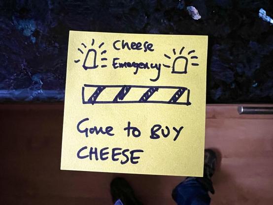 A yellow sticky note attached to a kitchen worktop. Test on it says "Cheese emergency: gone to BUY CHEESE", with little cartoon emergency alarm lights flashing in the corners