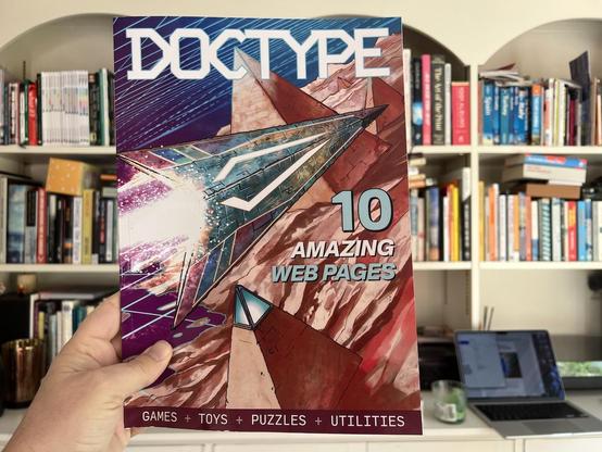 A copy of DOCTYPE magazine held in my hand in front of a crowded bookshelf