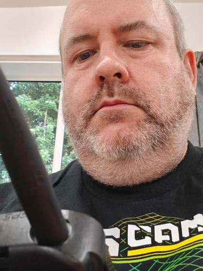 A picture of an incredibly handsome amateur radio operator from the UK, holding a radio whilst wearing a rather fetching OggCamp 2026 t-shirt.